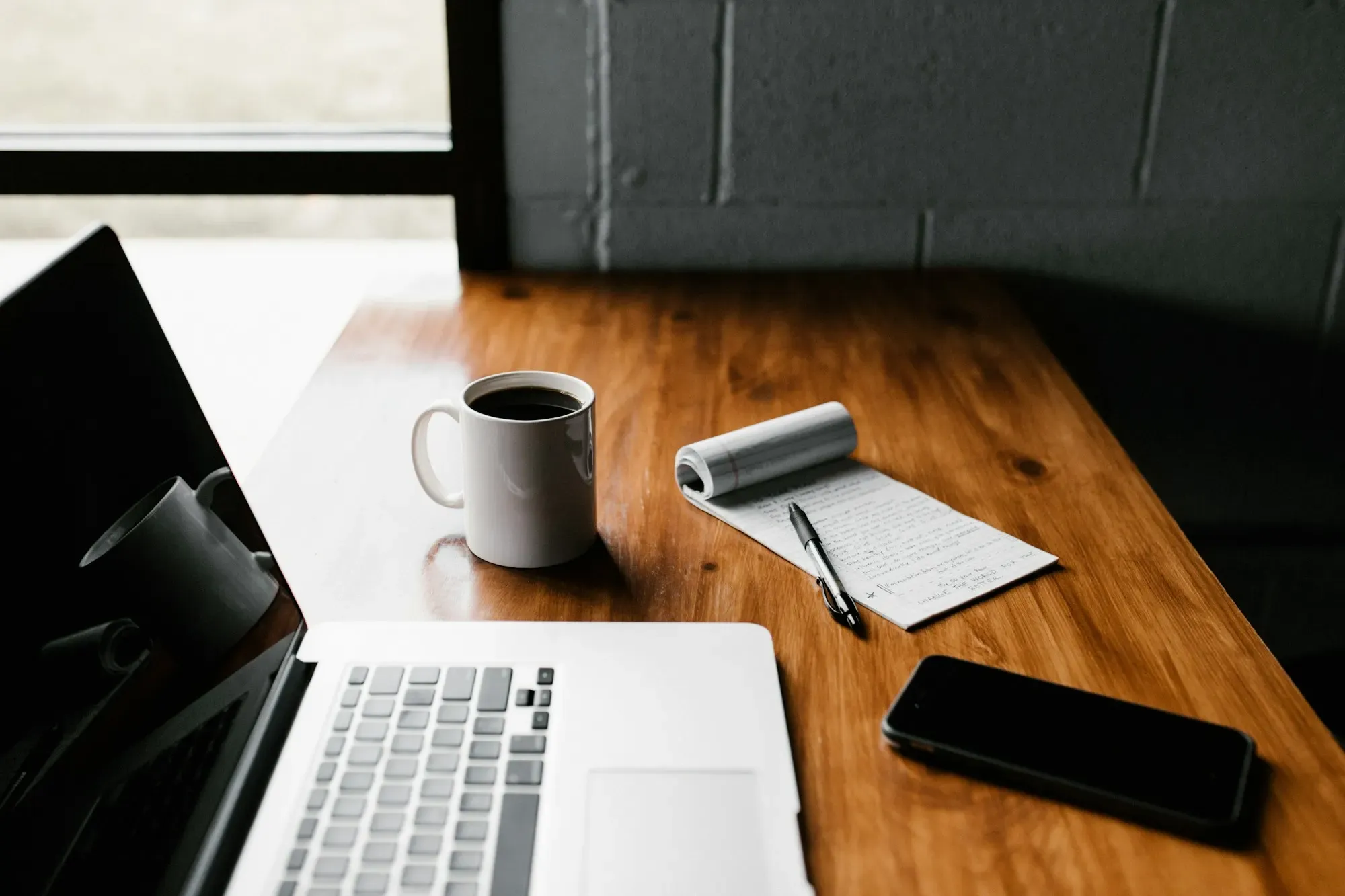 Laptop, cuaderno, café y celular sobre una mesa de madera
